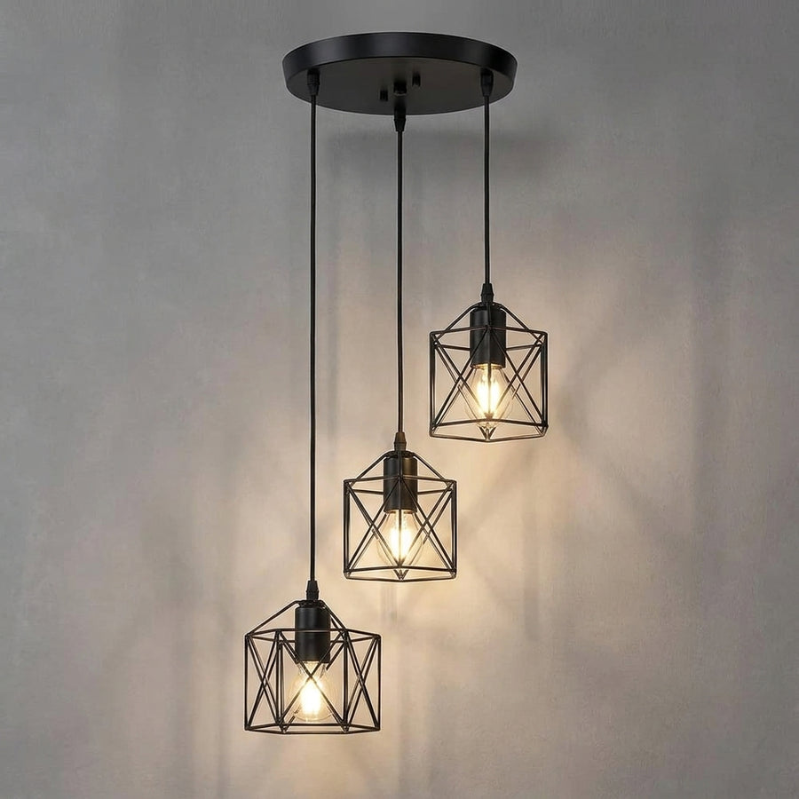 Three-light linear pendant ceiling fixture with a matte black metal frame and warm glowing Edison bulbs, shown against a neutral gray wall.