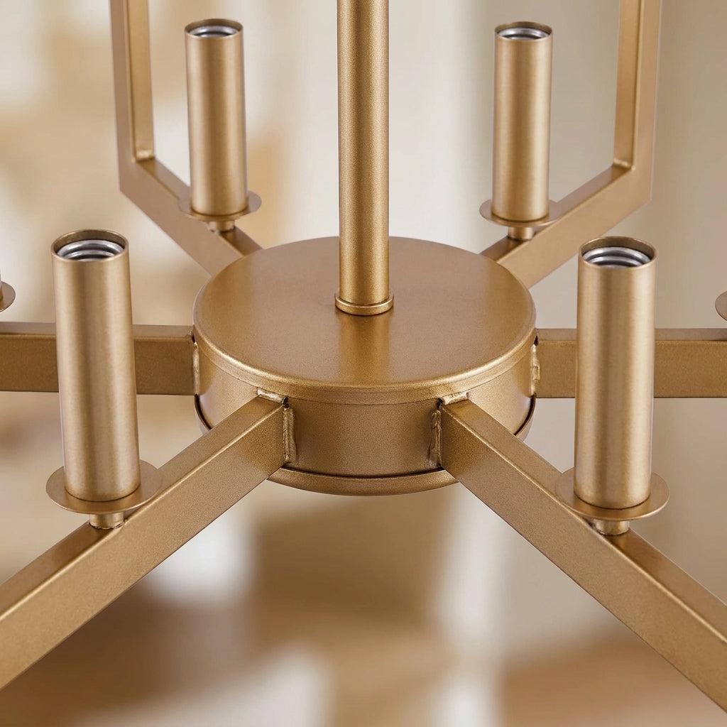 Close-up of a modern six-light chandelier with a brushed gold finish, showing the central round canopy, vertical downrod, and radial arms ending in cylindrical candle-style shades.