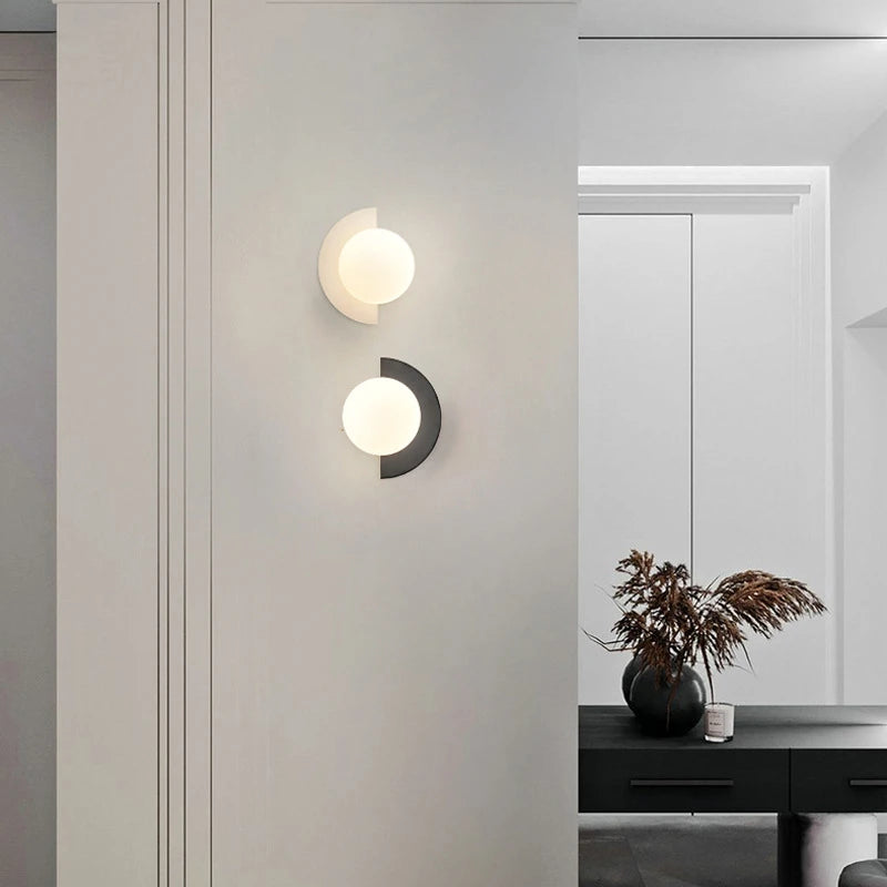 Modern wall sconces on a light gray wall with a mirror and plant in the background.