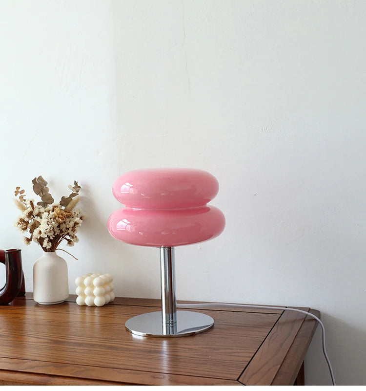 Pink table lamp on a wooden surface with decorative items in the background
