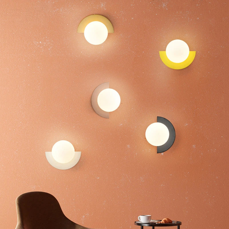 Five wall lights on a peach-colored wall with a chair and small table in the foreground.