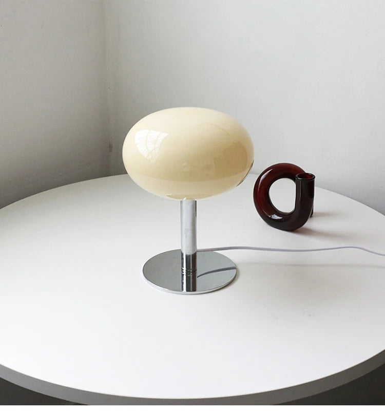 Modern table lamp with a white shade and chrome base on a round white table.